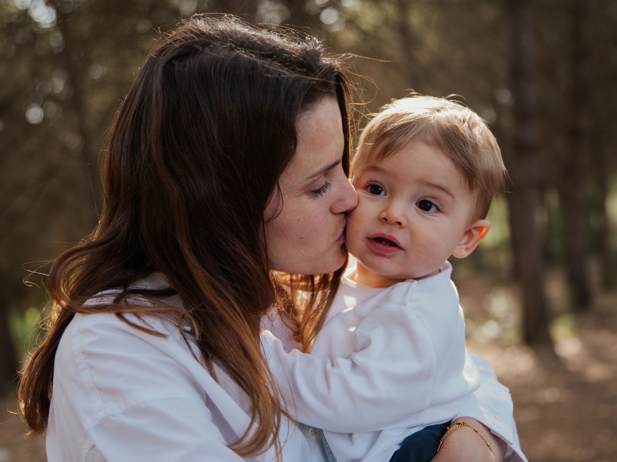 Madre besando a su bebé durante una sesión de fotos familiar en exterior